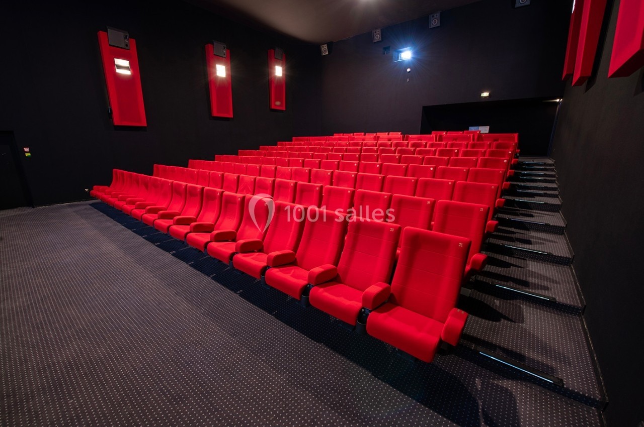 Salle de cinéma vide avec des rangées de sièges rouges et un éclairage tamisé.