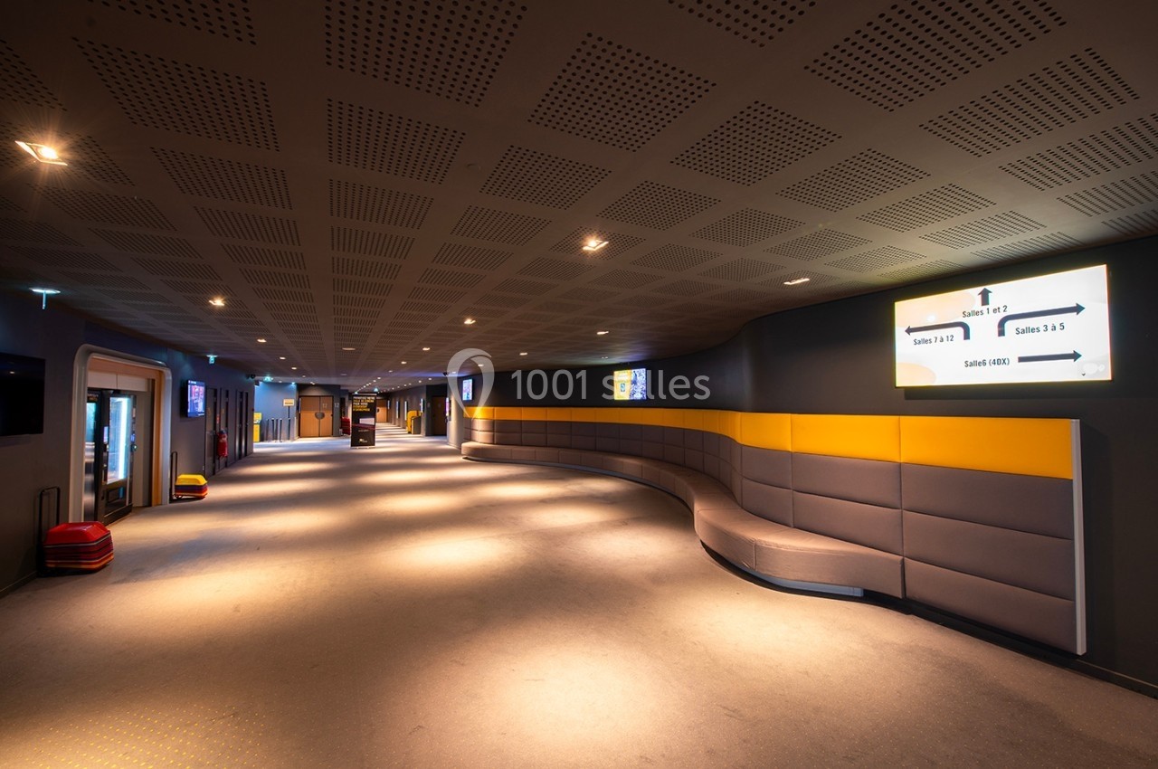 Couloir moderne avec éclairage tamisé, panneaux d'indication lumineux et banquettes grises le long du mur.