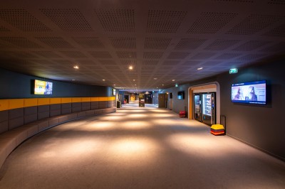 Couloir moderne avec éclairage tamisé, sièges incurvés, distributeurs automatiques et écrans muraux.
