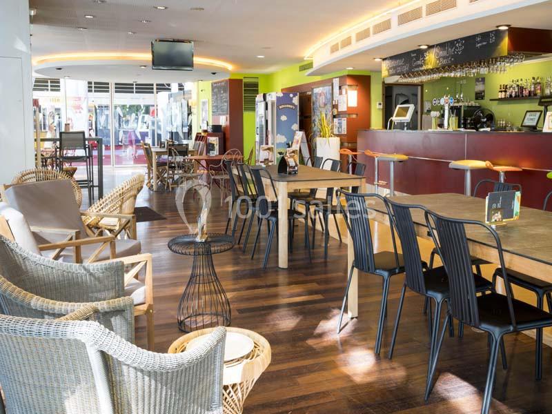 Salle de restaurant lumineuse avec mobilier en bois et métal, comptoir de bar rouge et décoration moderne.