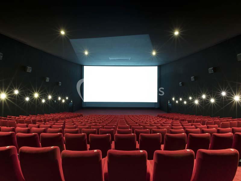 Salle de cinéma vide avec des rangées de fauteuils rouges et un grand écran blanc allumé.