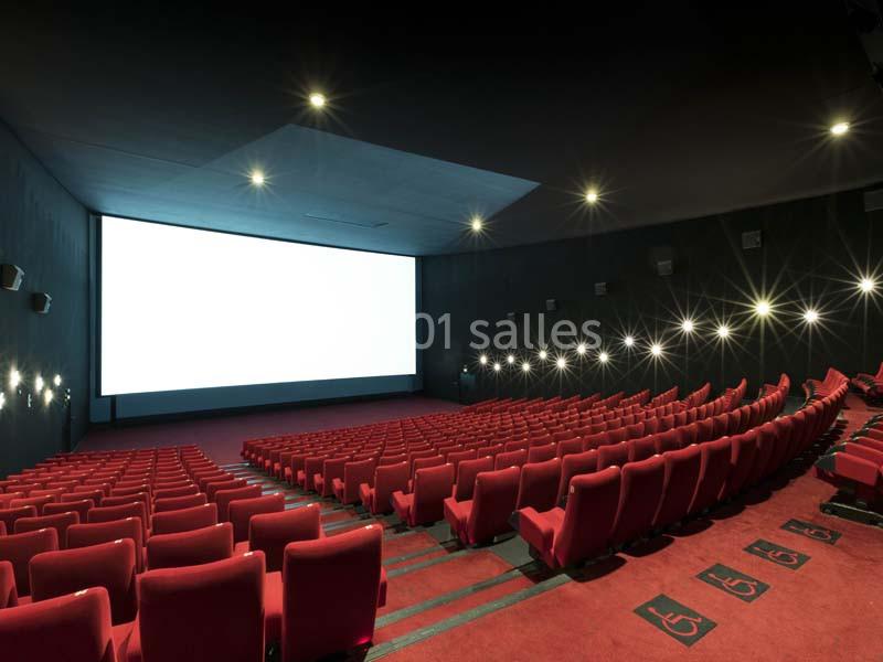Salle de cinéma vide avec des rangées de fauteuils rouges et un grand écran blanc allumé.
