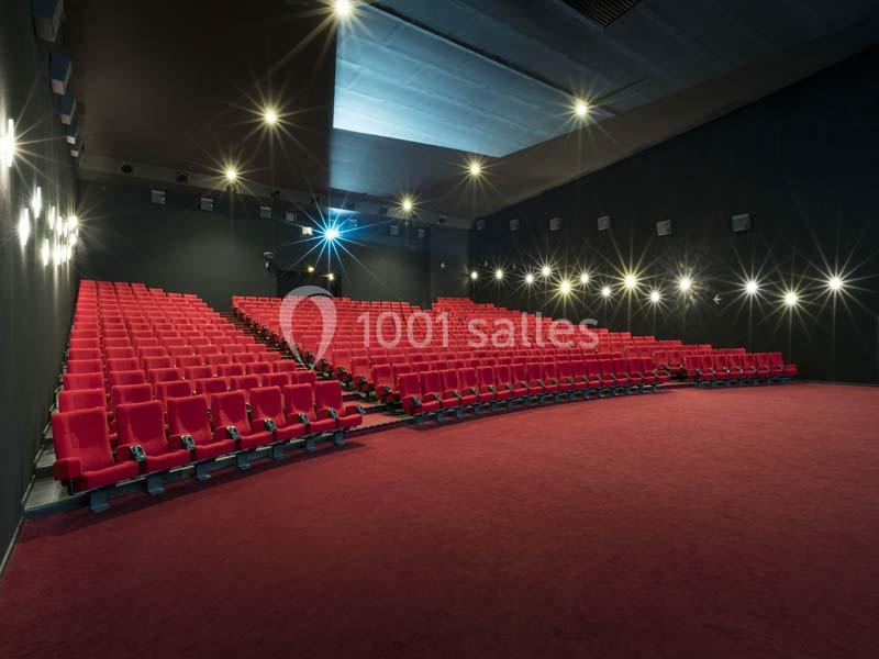 Salle de cinéma vide avec des rangées de sièges rouges et un éclairage tamisé.