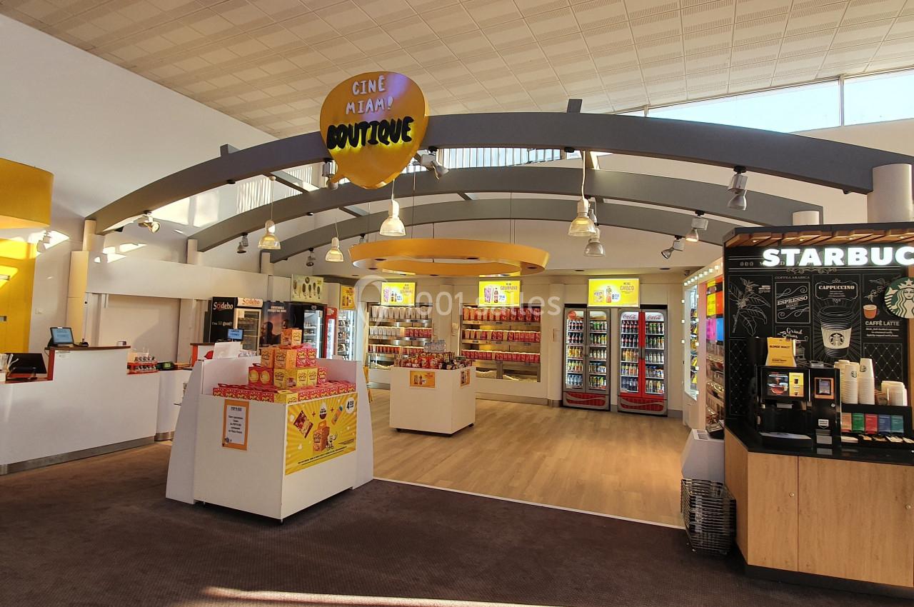 Hall lumineux avec comptoirs de vente, espace Starbucks et présentoirs de snacks dans un cinéma Pathé.