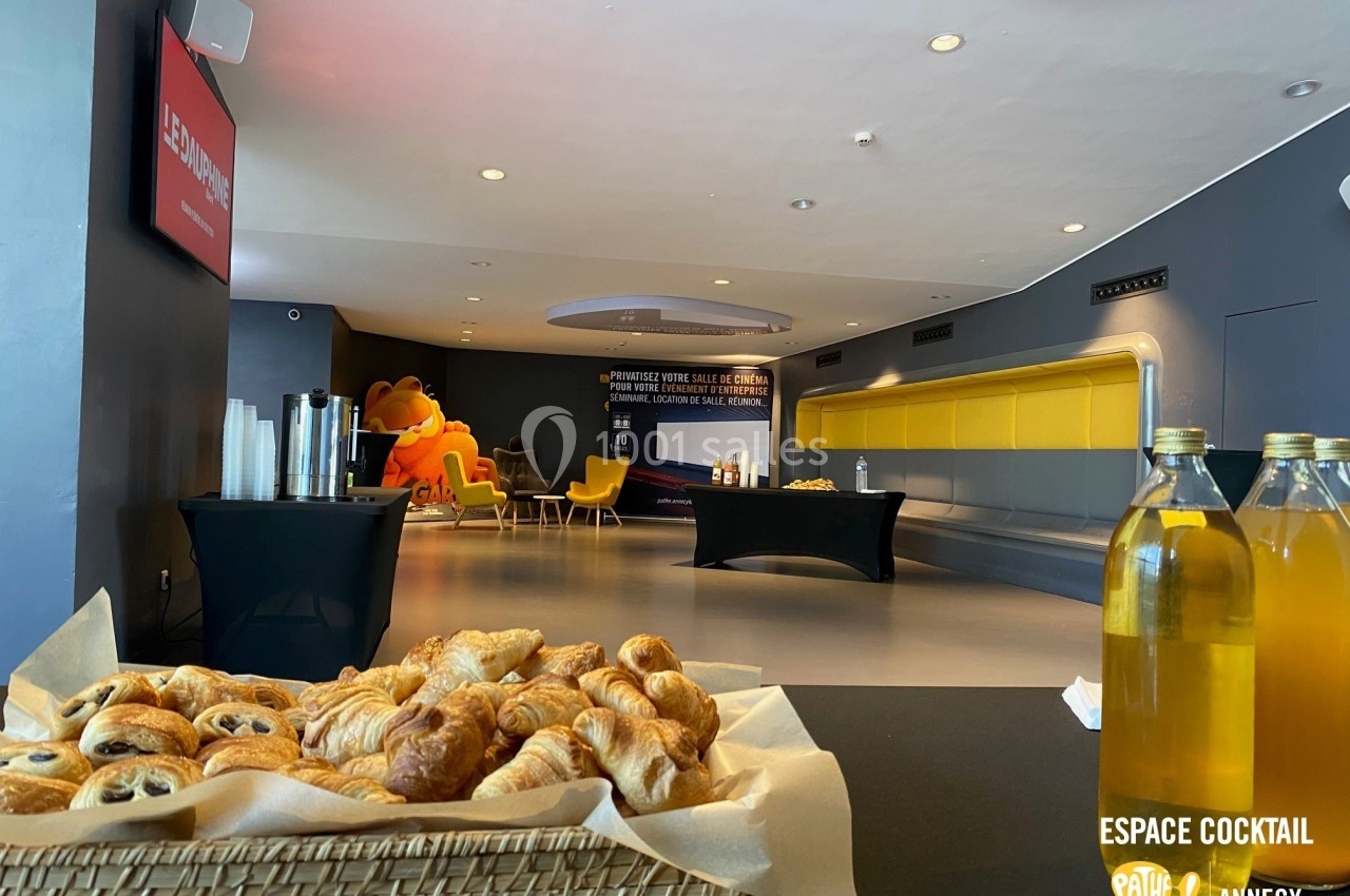 Plateau de viennoiseries au premier plan dans une salle moderne avec tables, chaises et boissons en arrière-plan.