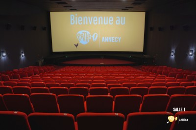 Rangées de sièges rouges alignés dans une salle de cinéma vide, éclairée par une lumière tamisée.