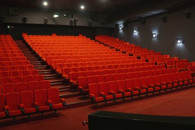 Rangées de sièges rouges alignés dans une salle de cinéma vide, éclairée par une lumière tamisée.