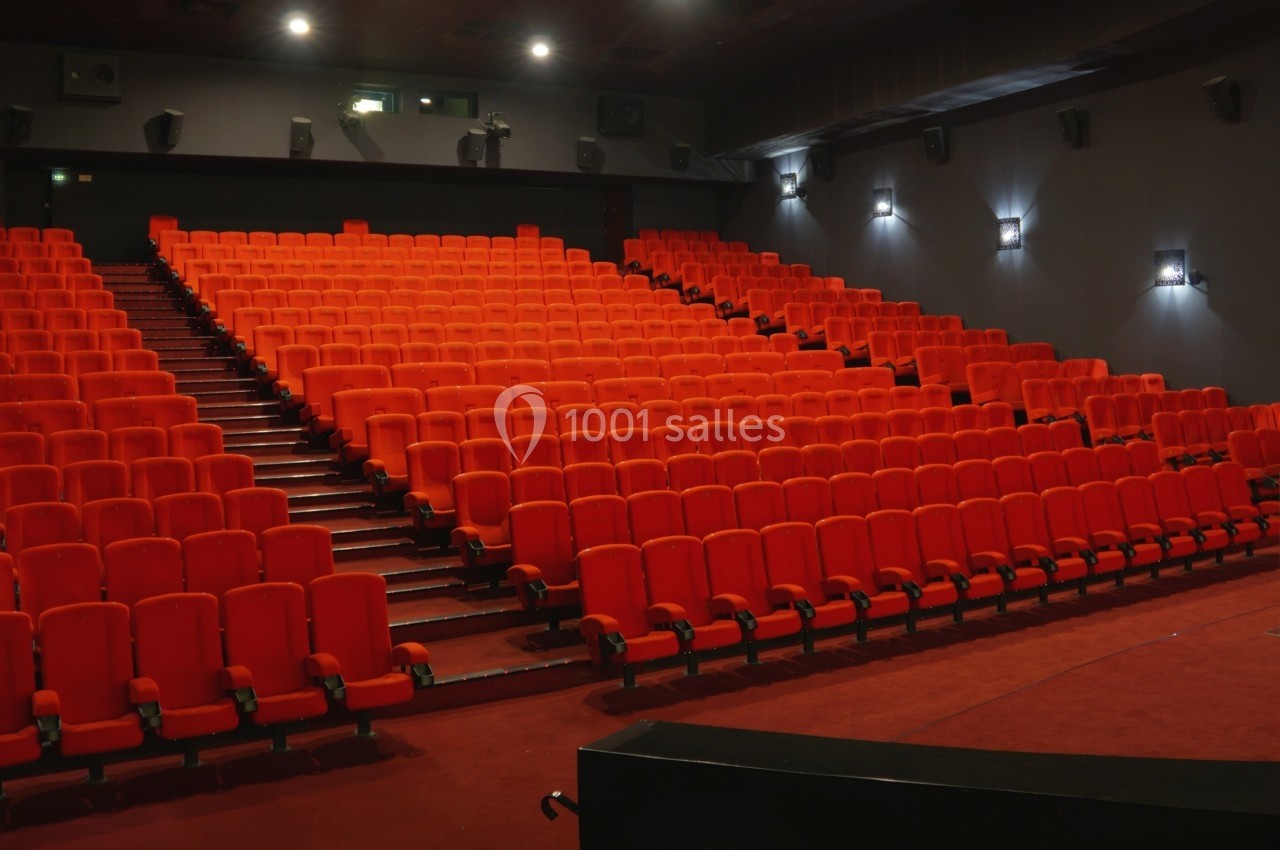 Salle de cinéma vide avec des rangées de sièges rouges et un éclairage mural tamisé.