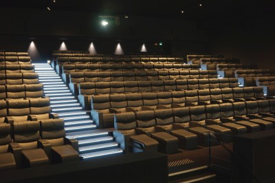 Rangées de sièges rouges alignés dans une salle de cinéma vide, éclairée par une lumière tamisée.