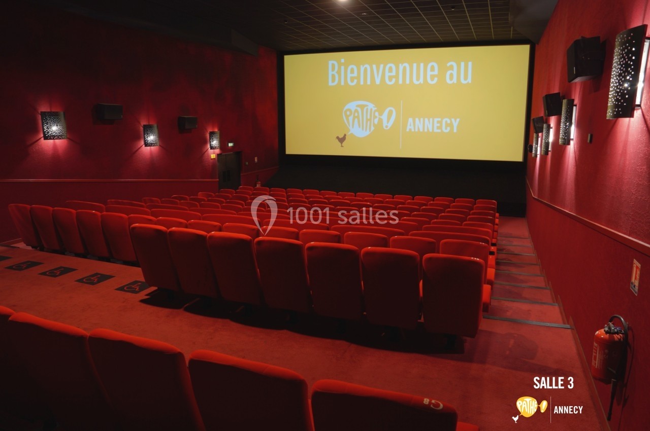 Salle de cinéma vide avec des rangées de fauteuils rouges et un écran affichant ’Bienvenue au Pathé Annecy’.