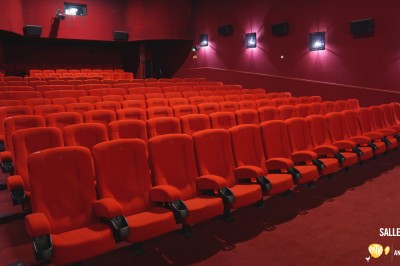 Rangées de sièges rouges alignés dans une salle de cinéma vide, éclairée par une lumière tamisée.