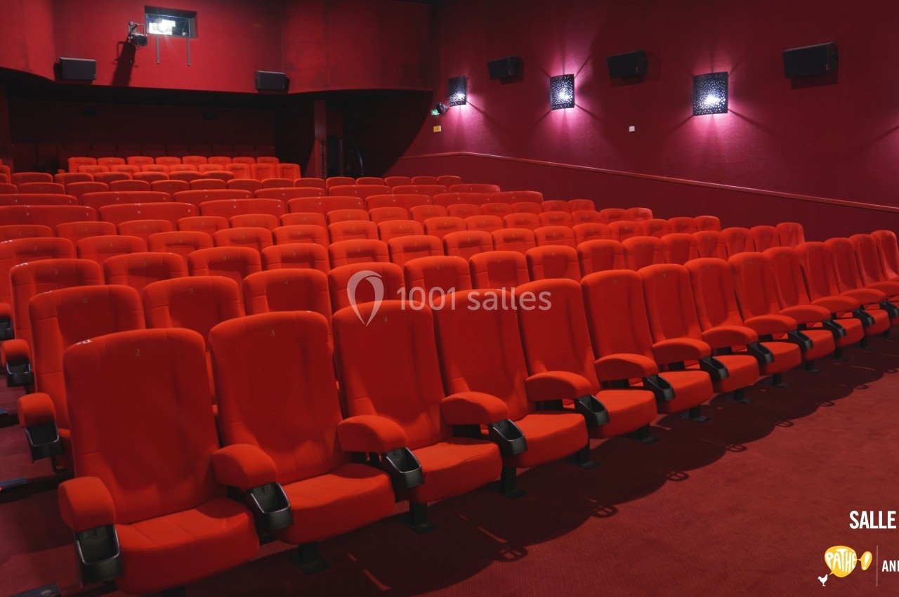 Salle de cinéma vide avec des rangées de fauteuils rouges alignés dans un espace sombre.