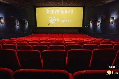 Rangées de sièges rouges alignés dans une salle de cinéma vide, éclairée par une lumière tamisée.