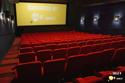 Rangées de sièges rouges alignés dans une salle de cinéma vide, éclairée par une lumière tamisée.