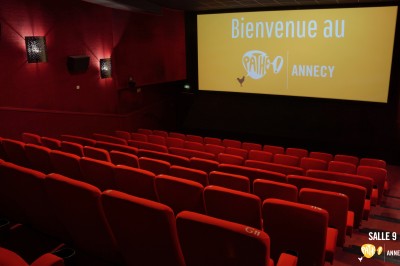 Rangées de sièges rouges alignés dans une salle de cinéma vide, éclairée par une lumière tamisée.