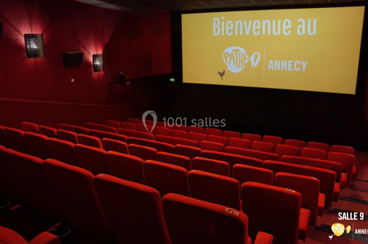 Salle de cinéma vide avec des sièges rouges et un écran affichant ’Bienvenue au Pathé Annecy’.