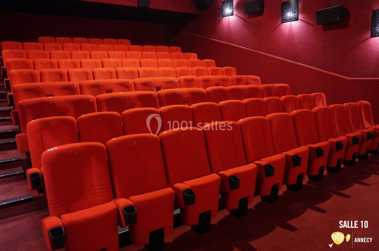 Rangées de sièges rouges alignés dans une salle de cinéma vide, éclairée par une lumière tamisée.