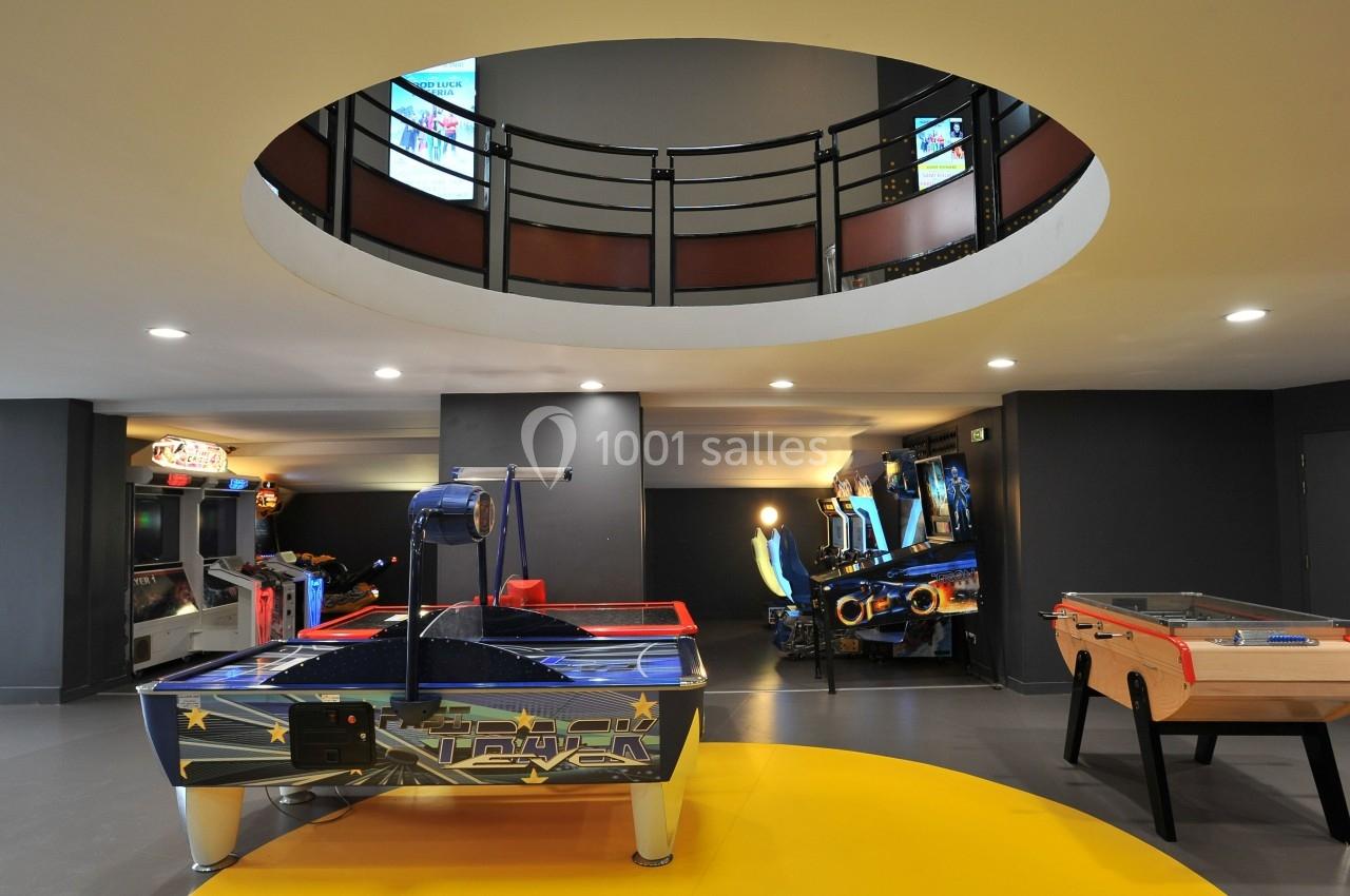 Salle de jeux avec un air hockey, un baby-foot et des bornes d'arcade sous un plafond circulaire ouvert.