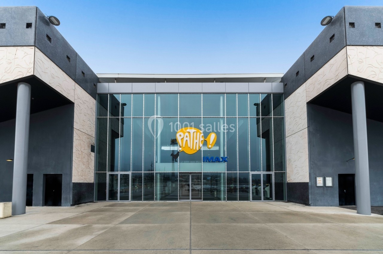 Façade vitrée d'un cinéma avec le logo Pathé et IMAX, entourée de murs gris et d'un sol en béton.
