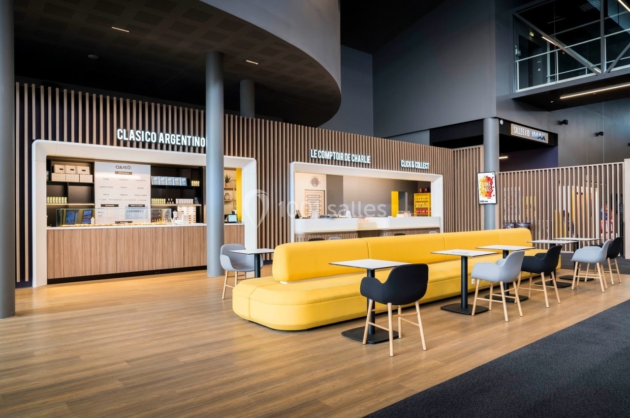 Espace de restauration moderne avec comptoirs lumineux, banquette jaune et chaises noires et grises.