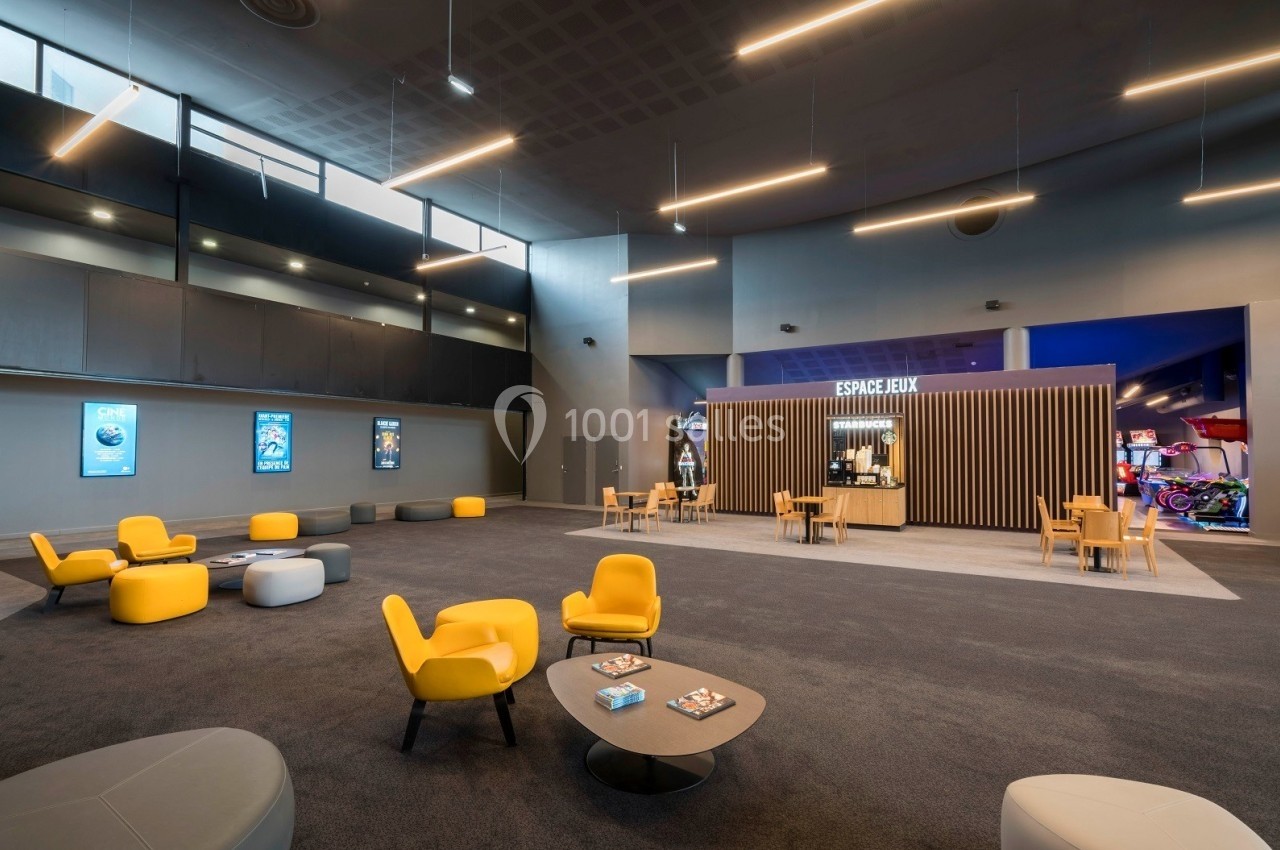 Espace intérieur moderne avec fauteuils jaunes, tables basses, affiches murales et un comptoir marqué ’Espace Jeux’.