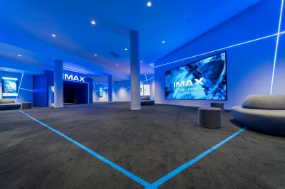 Salle de cinéma moderne avec des rangées de sièges rouges et un grand écran blanc allumé.