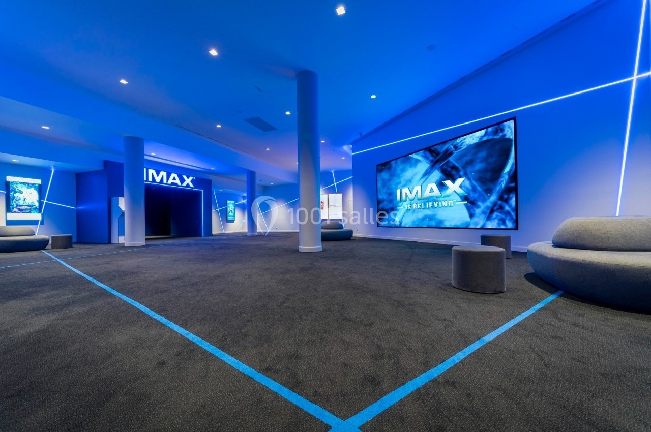 Salle de cinéma moderne avec éclairage bleu, écrans IMAX et sièges minimalistes.