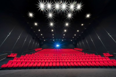 Salle de cinéma moderne avec des rangées de sièges rouges et un grand écran blanc allumé.