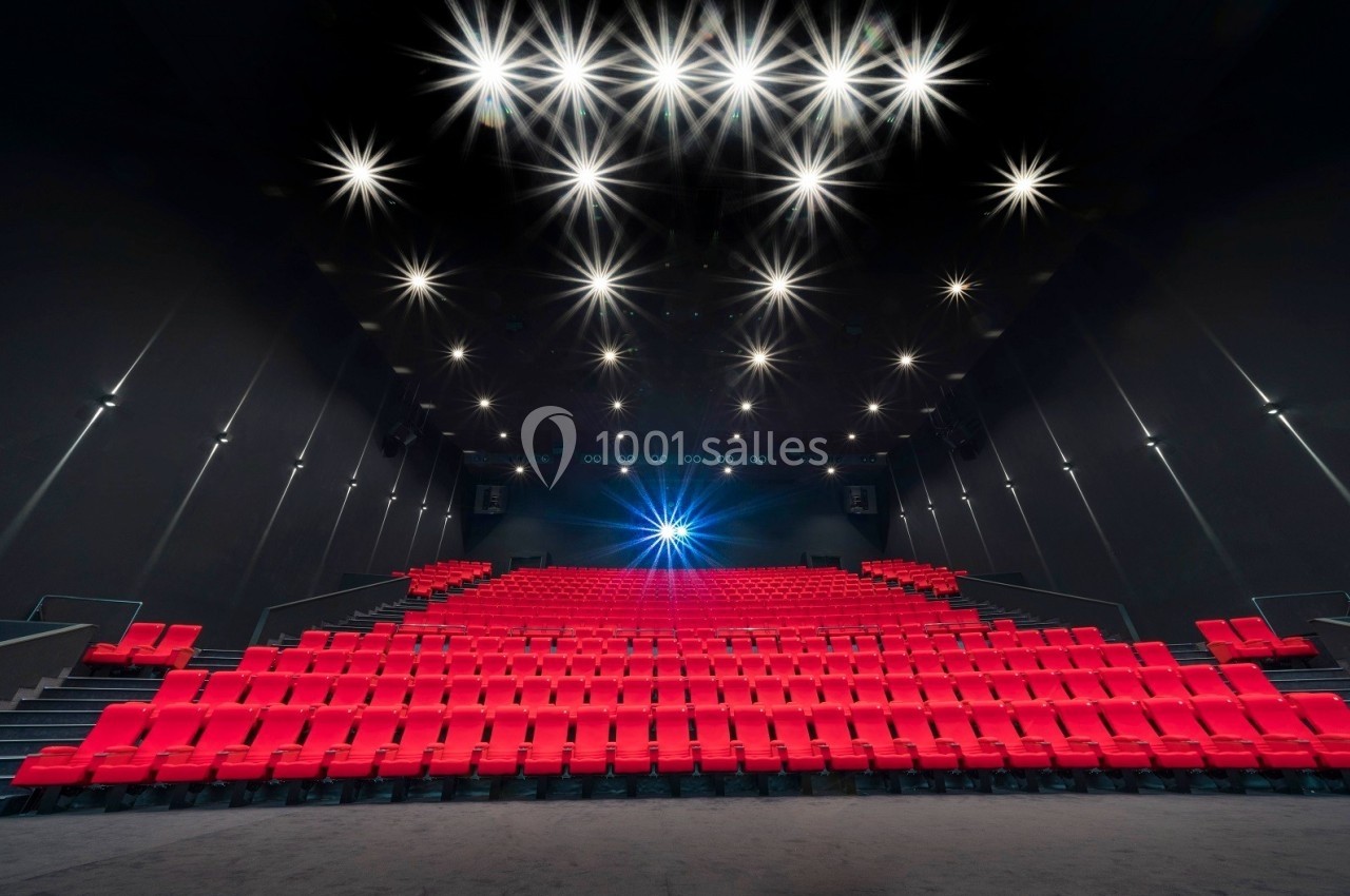 Salle de cinéma vide avec des rangées de sièges rouges et un éclairage lumineux au plafond.