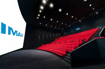Salle de cinéma moderne avec des rangées de sièges rouges et un grand écran blanc allumé.