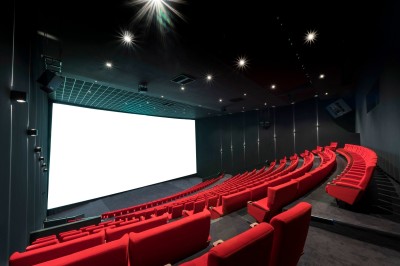 Salle de cinéma moderne avec des rangées de sièges rouges et un grand écran blanc allumé.
