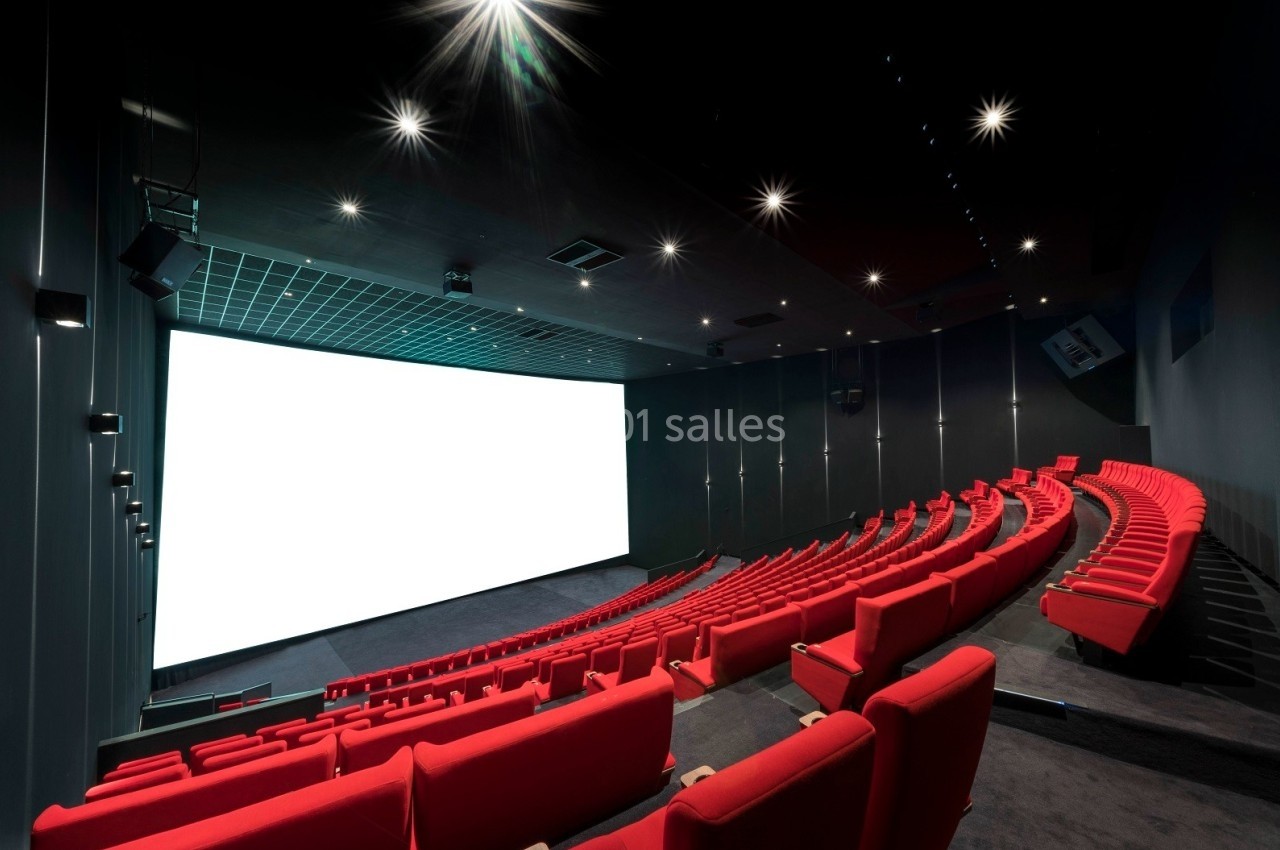 Salle de cinéma moderne avec des rangées de sièges rouges et un grand écran blanc allumé.