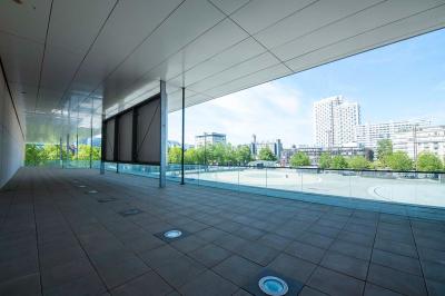Salle lumineuse avec murs jaunes et gris, mobilier moderne espacé, grandes fenêtres laissant entrer la lumière naturelle.