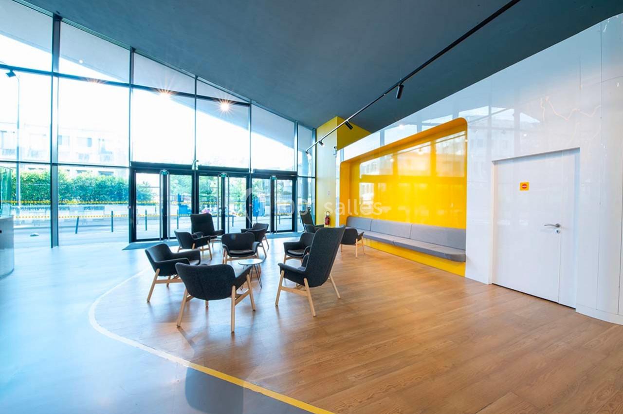 Espace lumineux avec des fauteuils noirs, un mur jaune vif, un sol en bois et de grandes baies vitrées donnant sur l…