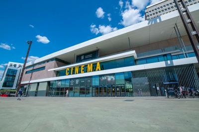 Salle lumineuse avec murs jaunes et gris, mobilier moderne espacé, grandes fenêtres laissant entrer la lumière naturelle.