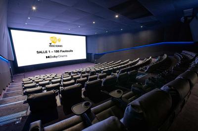 Salle lumineuse avec murs jaunes et gris, mobilier moderne espacé, grandes fenêtres laissant entrer la lumière naturelle.