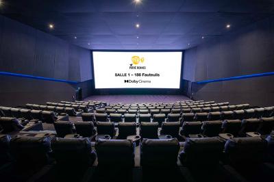 Salle lumineuse avec murs jaunes et gris, mobilier moderne espacé, grandes fenêtres laissant entrer la lumière naturelle.
