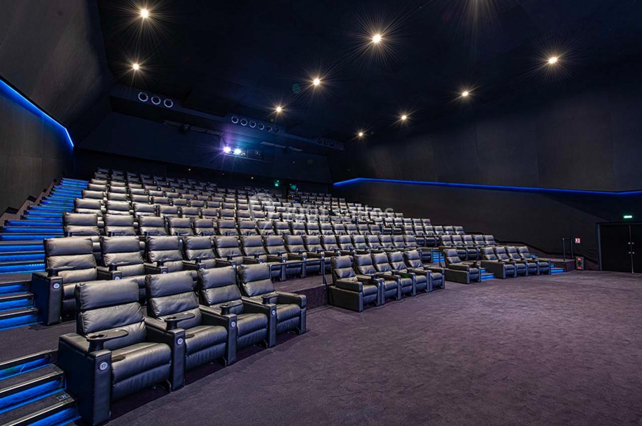 Salle de cinéma vide avec des fauteuils en cuir noir, éclairage tamisé et allées illuminées.