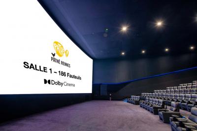 Salle lumineuse avec murs jaunes et gris, mobilier moderne espacé, grandes fenêtres laissant entrer la lumière naturelle.