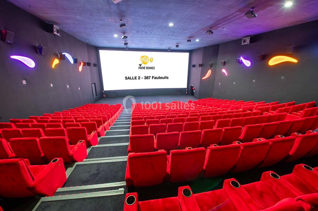 Salle de cinéma vide avec des rangées de fauteuils rouges et un écran affichant ’Salle 2 - 387 fauteuils’.