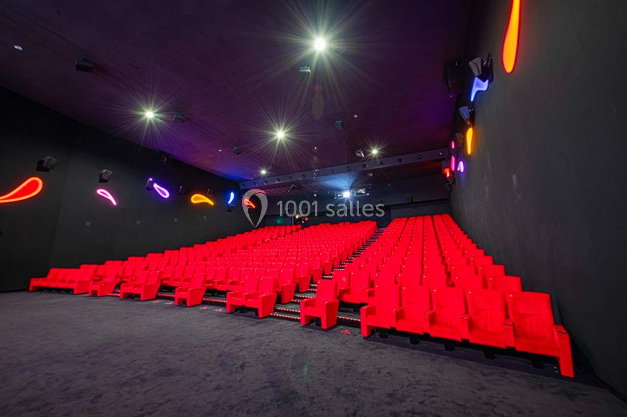 Salle de cinéma vide avec rangées de fauteuils rouges et éclairage néon coloré sur les murs sombres.
