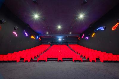 Salle lumineuse avec murs jaunes et gris, mobilier moderne espacé, grandes fenêtres laissant entrer la lumière naturelle.