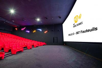 Salle lumineuse avec murs jaunes et gris, mobilier moderne espacé, grandes fenêtres laissant entrer la lumière naturelle.