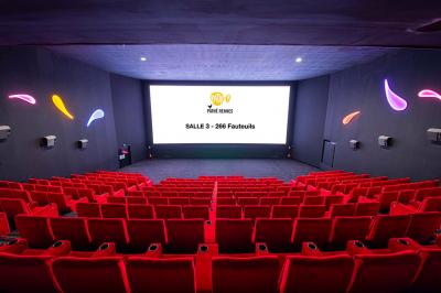 Salle lumineuse avec murs jaunes et gris, mobilier moderne espacé, grandes fenêtres laissant entrer la lumière naturelle.