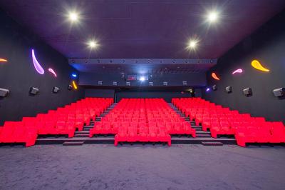 Salle lumineuse avec murs jaunes et gris, mobilier moderne espacé, grandes fenêtres laissant entrer la lumière naturelle.