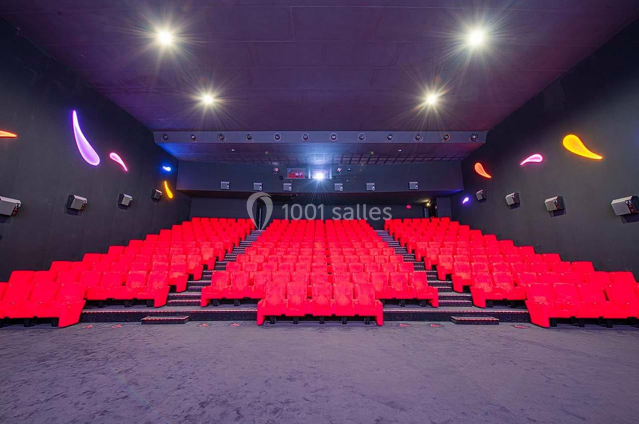 Salle de cinéma vide avec rangées de fauteuils rouges, éclairage tamisé et décorations murales lumineuses.