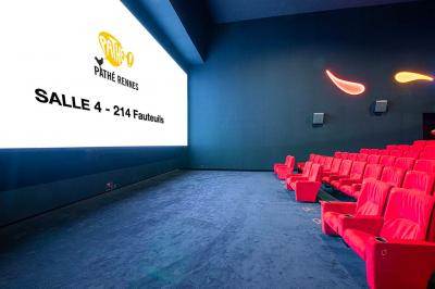 Salle lumineuse avec murs jaunes et gris, mobilier moderne espacé, grandes fenêtres laissant entrer la lumière naturelle.