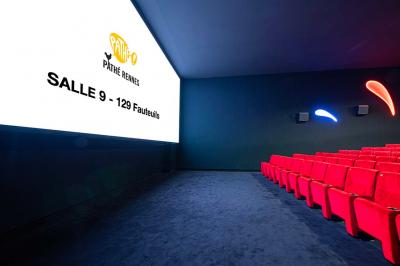 Salle lumineuse avec murs jaunes et gris, mobilier moderne espacé, grandes fenêtres laissant entrer la lumière naturelle.