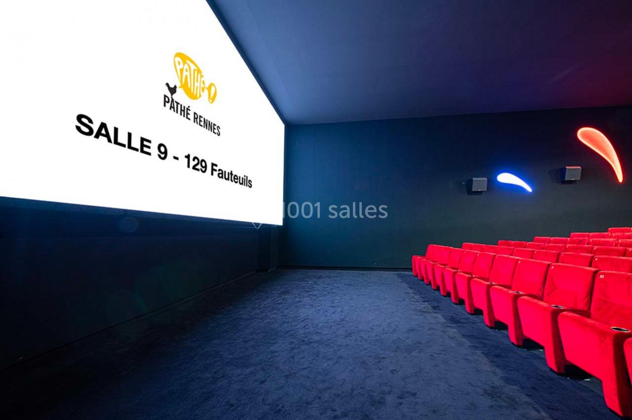 Salle de cinéma moderne avec écran allumé, sièges rouges alignés et éclairage mural discret.