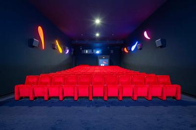 Salle lumineuse avec murs jaunes et gris, mobilier moderne espacé, grandes fenêtres laissant entrer la lumière naturelle.